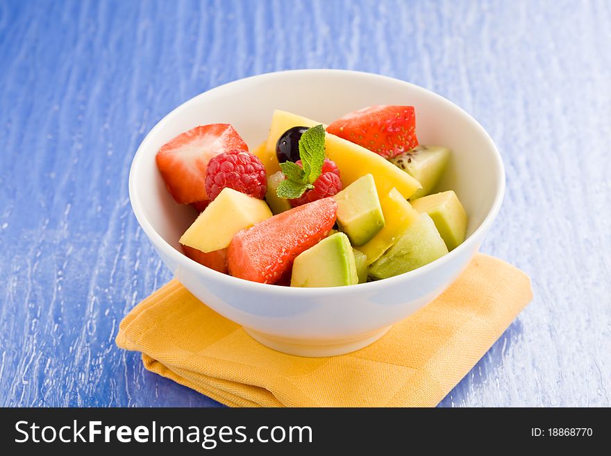 Photo of colorful fruit salad on blue glass table with small mint leaf