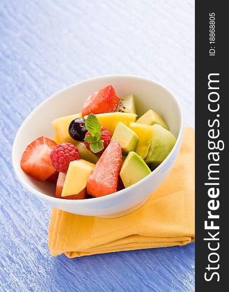 Photo of colorful fruit salad on blue glass table with small mint leaf