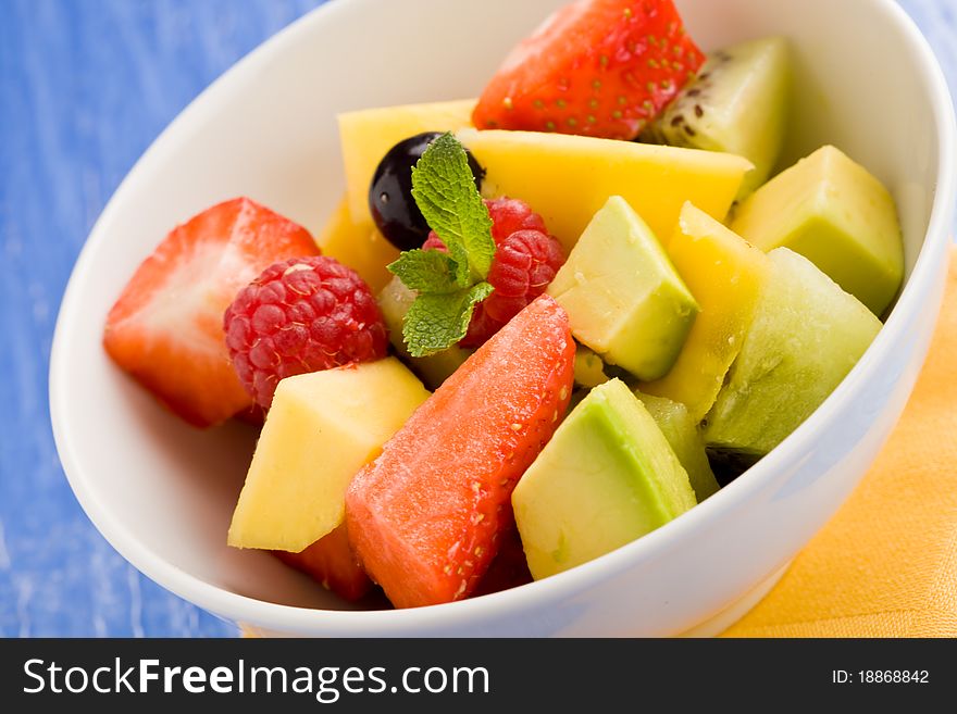 Photo of colorful fruit salad on blue glass table with small mint leaf