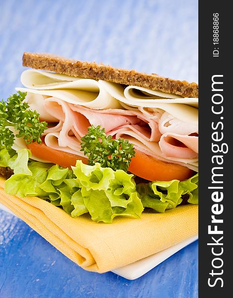 Photo of delicious big cheese and ham sandwich with lettuce on blue glass table