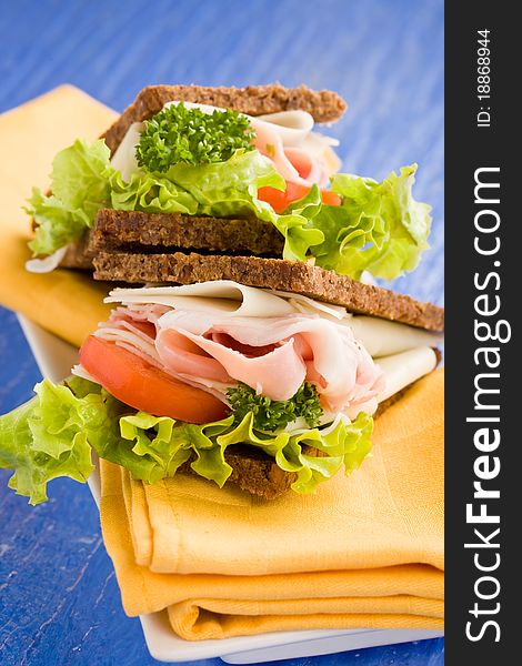 Photo of delicious big cheese and ham sandwich with lettuce on blue glass table