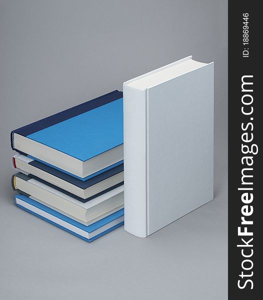A plain white book standing with several other books behind on a grey background ideal for graphic design. A plain white book standing with several other books behind on a grey background ideal for graphic design
