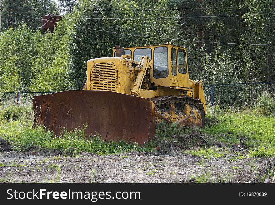 Big old yellow rusty tractor in the field, among the green grass