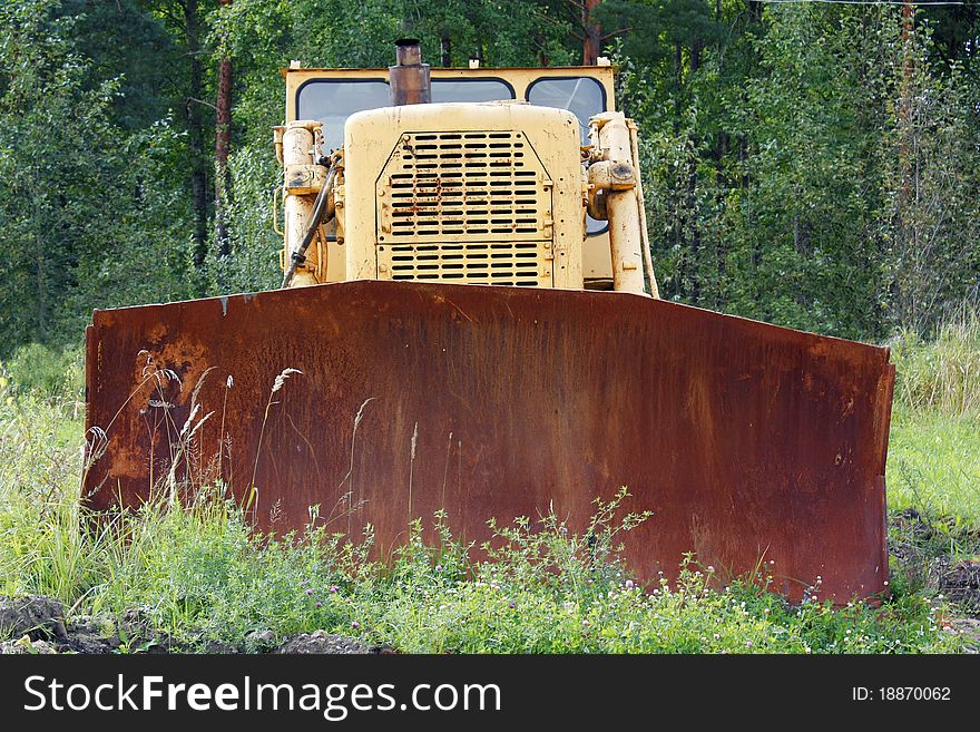 Big old yellow rusty tractor in the field, among the green grass