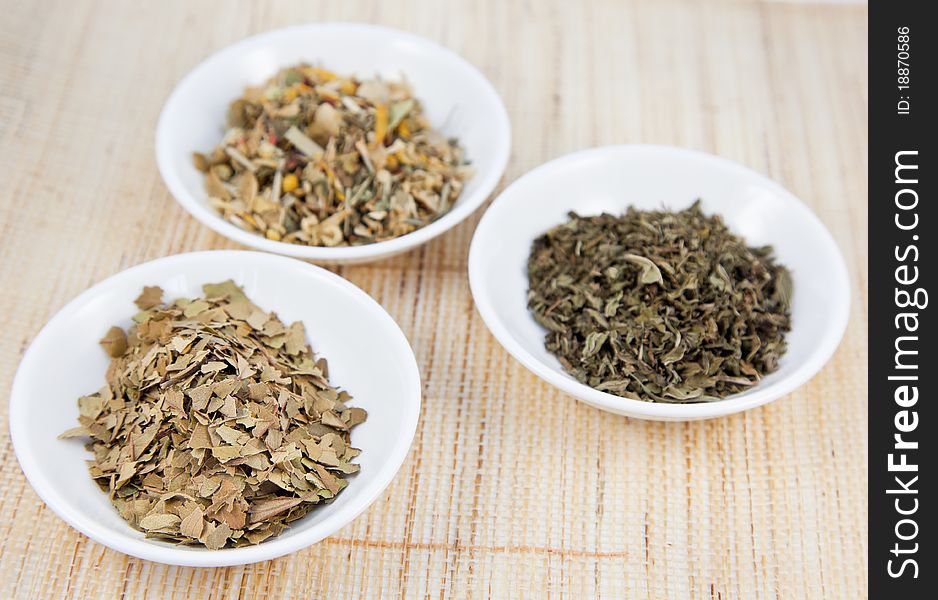 Herbal teas in small white bowls on natual matting, focus on front left tea.