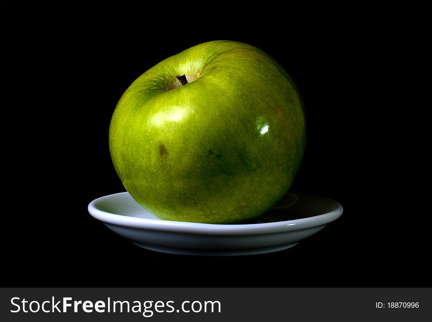 Green apple on a plate on black background