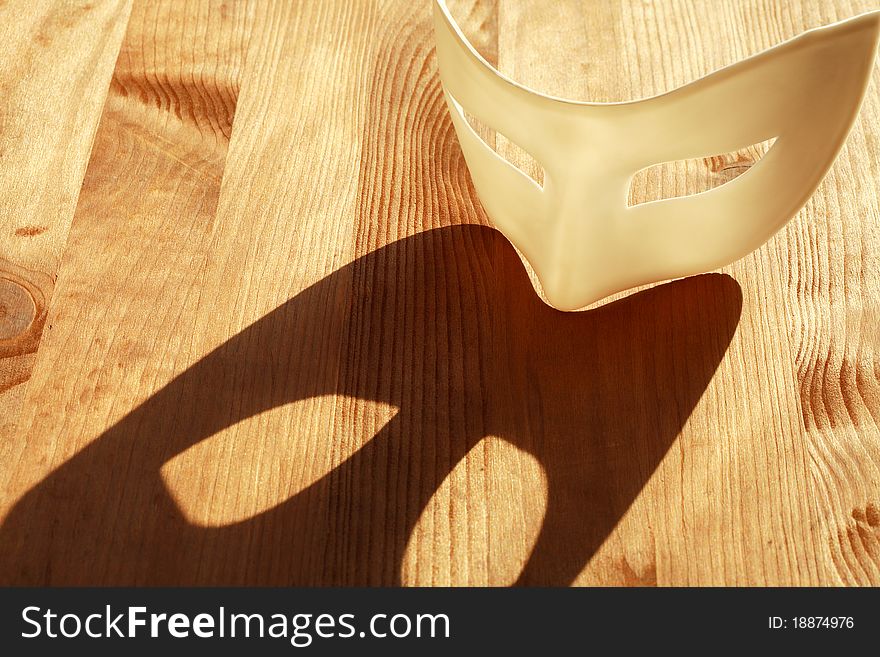 White plastic venetian mask lying on wooden surface with sunbeam and shadow. White plastic venetian mask lying on wooden surface with sunbeam and shadow