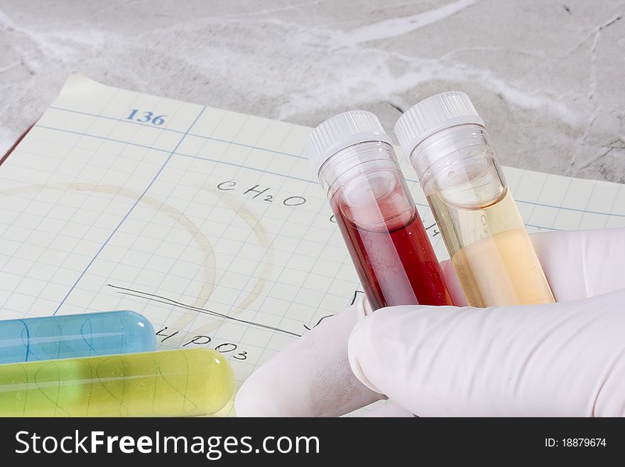 Hand holding test tubes in front of a laboratory notebook. Hand holding test tubes in front of a laboratory notebook.