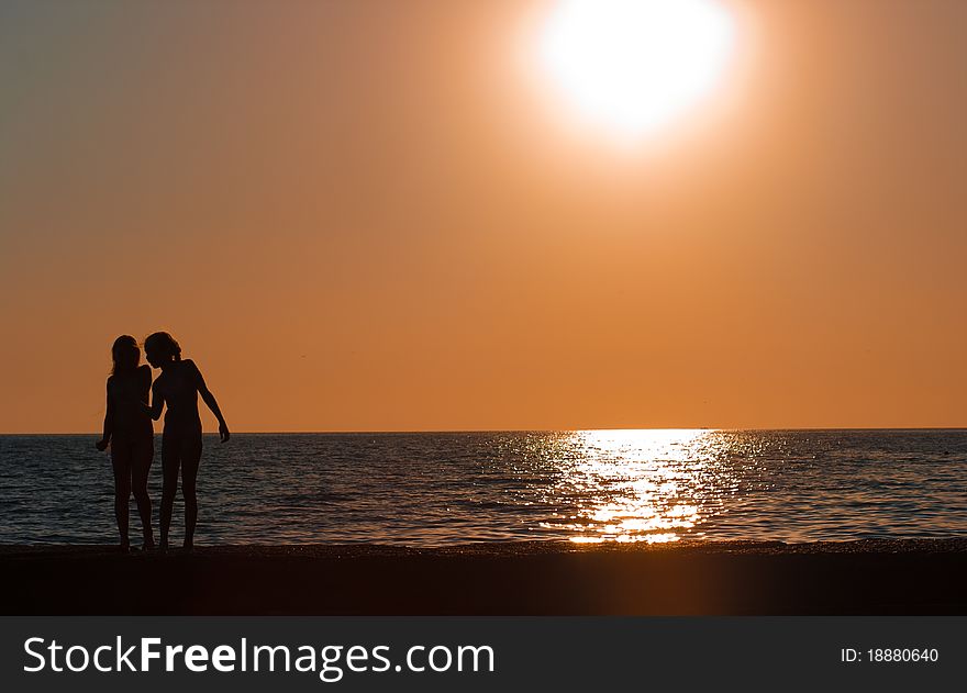 Girls silhouettes standing in front of sea or ocean on sunset