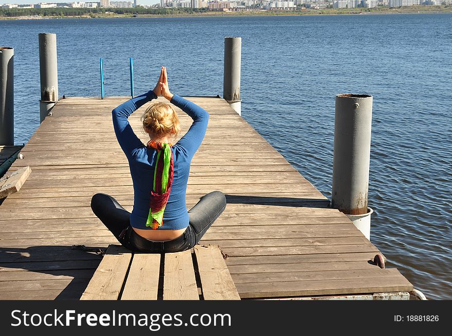 Fitness health, in coast, the girl spends his free time, she sits on the pier overlooking the water and city in the distance, close-up. Fitness health, in coast, the girl spends his free time, she sits on the pier overlooking the water and city in the distance, close-up