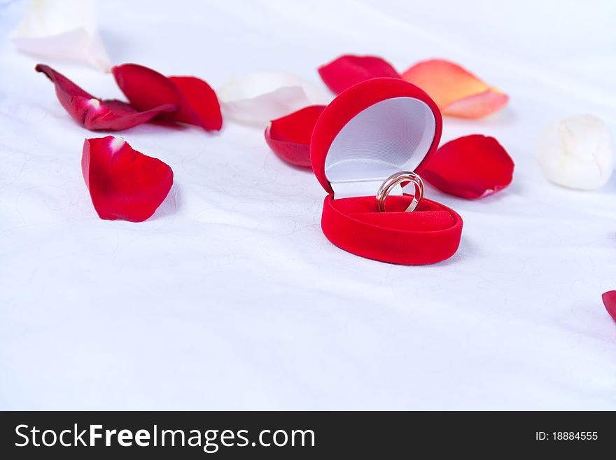 Wedding rings in the red box lie on the bed with rose petals
