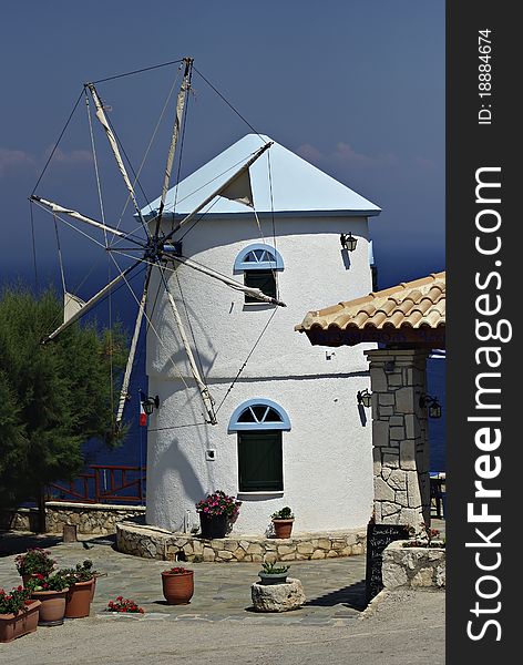 Traditional Greek windmill painted white with light blue roof at sunny summer day.