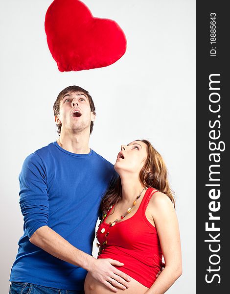 Surprised couple of young man and pregnant woman looking up at red heart