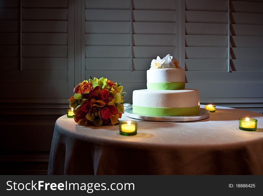 Green and White wedding cake on Table surrounded by candles and bride's bouquet