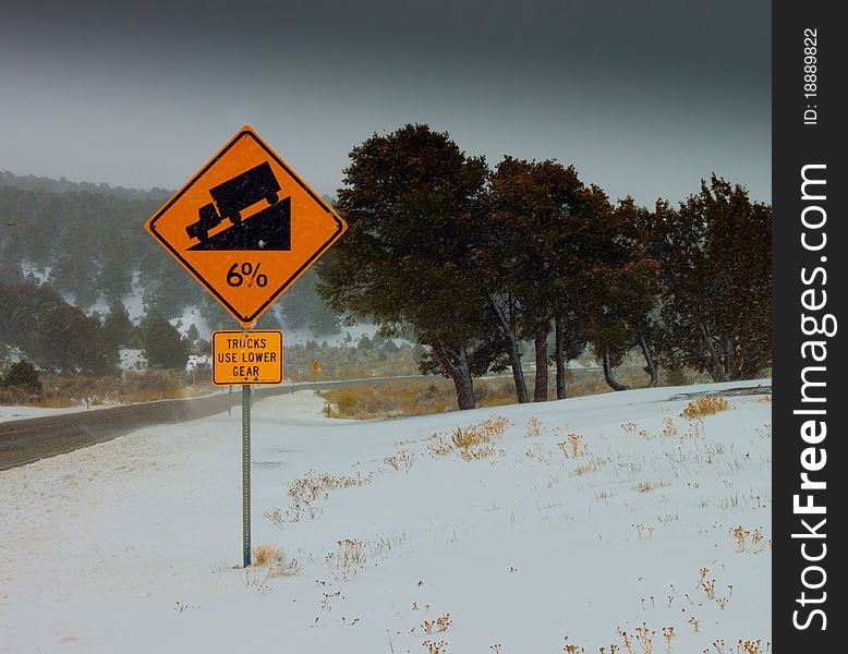 A photograph of a 6% Grade Sign. The sign states, Trucks Use Lower Gear. It is a snowy icy day on a windy road. A photograph of a 6% Grade Sign. The sign states, Trucks Use Lower Gear. It is a snowy icy day on a windy road.