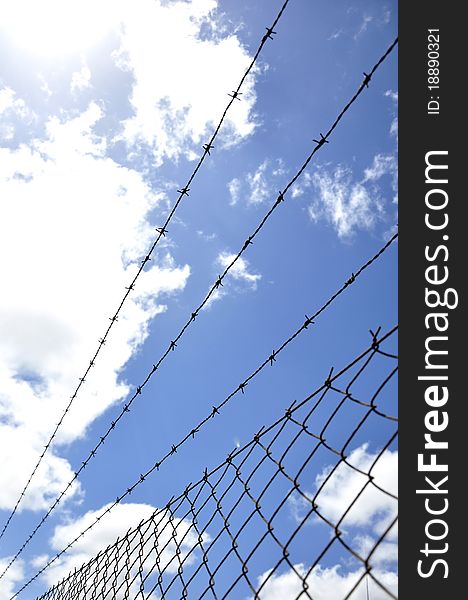 Fence of mesh with barbed wire under blue sky. Fence of mesh with barbed wire under blue sky