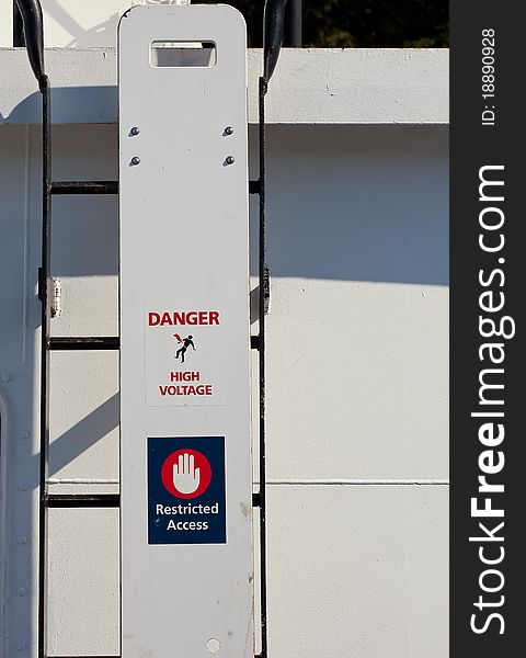Black rung ladder to upper deck on a passenger ship is barricaded with a metal plate labelled Danger High Voltage Restricted Access.