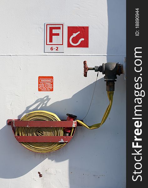 A coiled fire hose in metal cradle is connected to water supply valve at an emergency fire fighting location on a passenger ship. A coiled fire hose in metal cradle is connected to water supply valve at an emergency fire fighting location on a passenger ship.