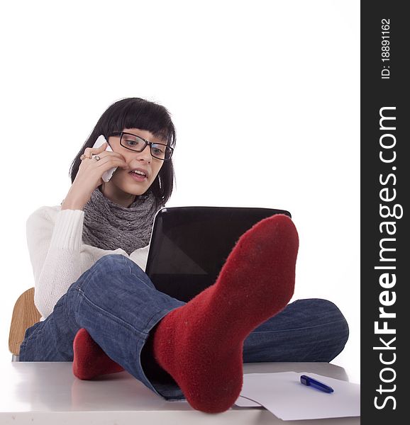 Brunette woman sits thrown feet on the desk and talking on the phone on white background. Brunette woman sits thrown feet on the desk and talking on the phone on white background