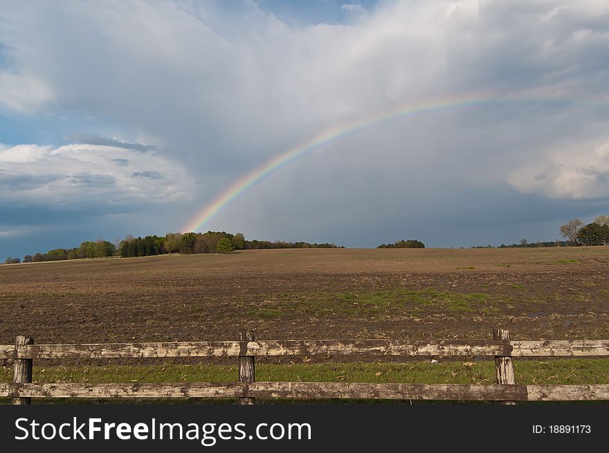 A rainbow and clouds cover the sky above a farm field. A rainbow and clouds cover the sky above a farm field.