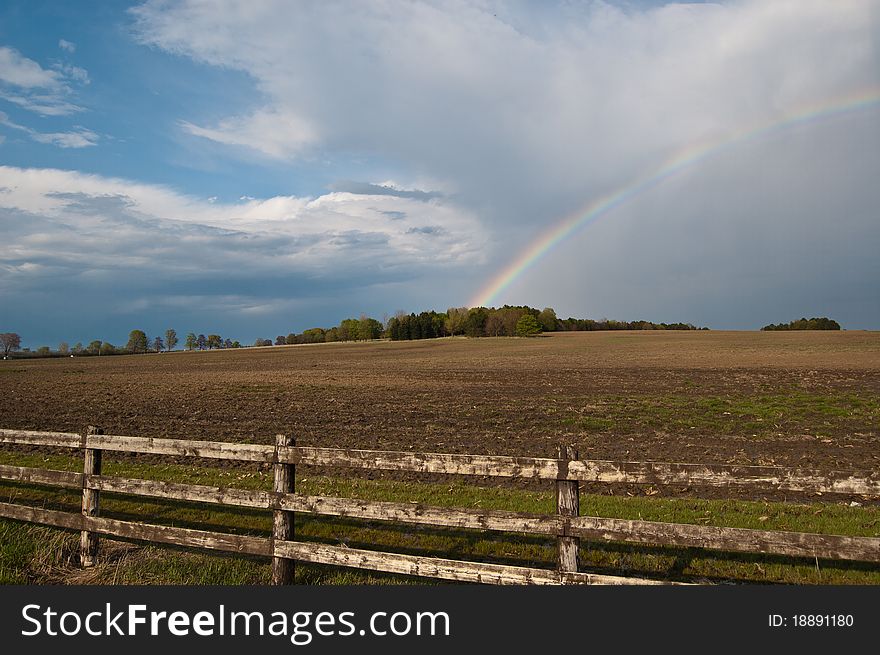 A rainbow and clouds cover the sky above a farm field. A rainbow and clouds cover the sky above a farm field.