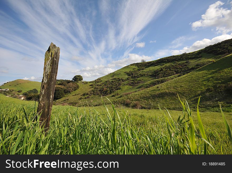 Field with grass, bushes, large fence post and dramic sky. Field with grass, bushes, large fence post and dramic sky