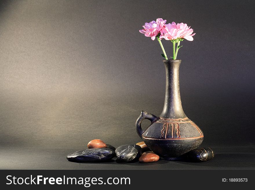 Ancient ceramic vase with nice pink flower near stones on dark background. Ancient ceramic vase with nice pink flower near stones on dark background