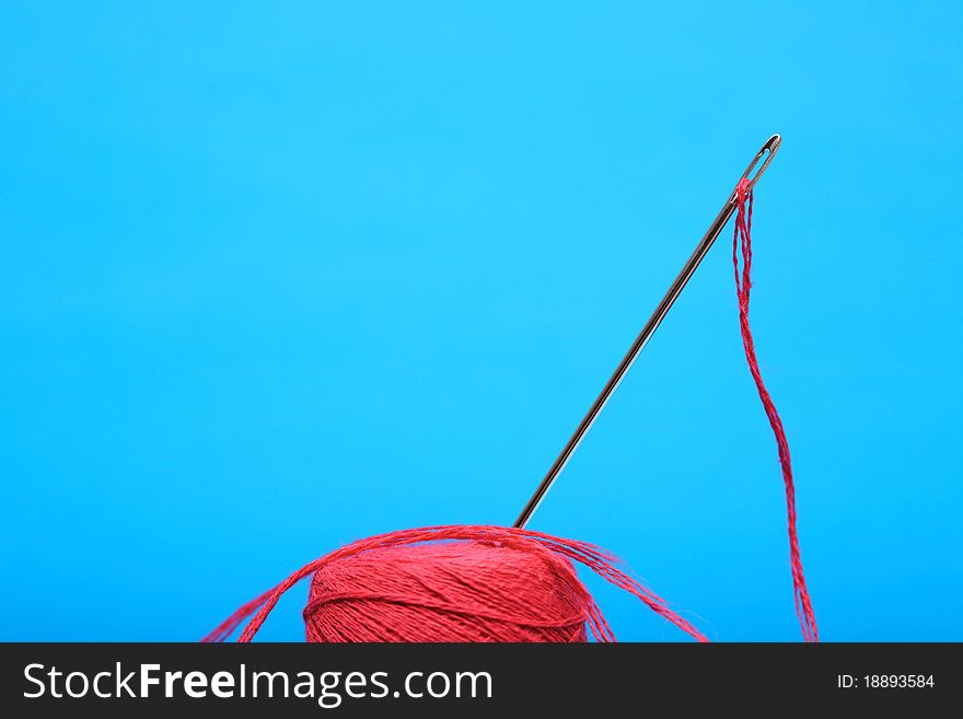 Extreme closeup of steel needle with red thread standing on blue background. Extreme closeup of steel needle with red thread standing on blue background