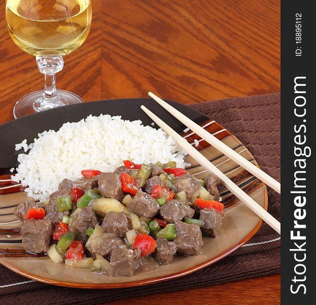 Sweet and sour beef with peppers on top of rice and glass of wine