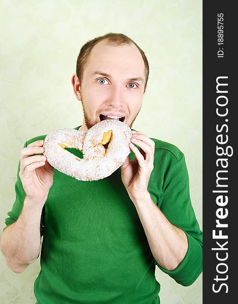 Man in green shirt biting big cracknel with white topping and looking at camera