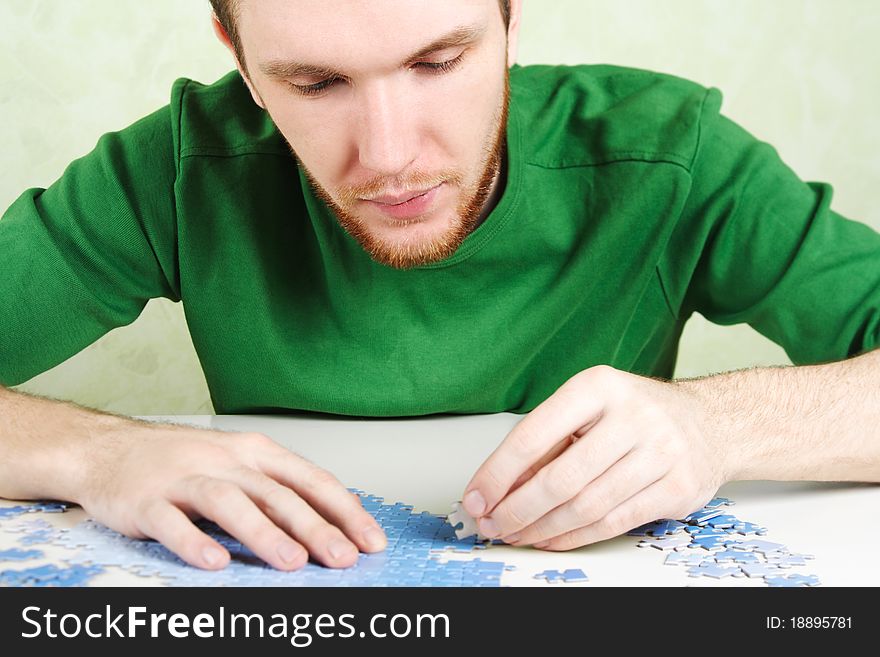 Man in green shirt assembling blue puzzle pieces. Man in green shirt assembling blue puzzle pieces