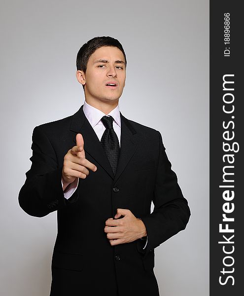 Young serious business man in black suit and tie. gray background