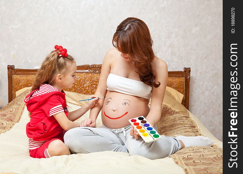 A daughter is painting on he rpregnant mother`s belly. A daughter is painting on he rpregnant mother`s belly