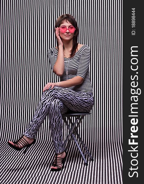 Cute girl in a striped clothes and pink sunglasses on the striped background