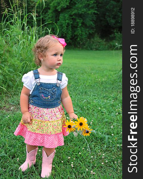 Pretty curly headed blonde toddler girl holding flowers outside wearing pink boots and a dress. Pretty curly headed blonde toddler girl holding flowers outside wearing pink boots and a dress