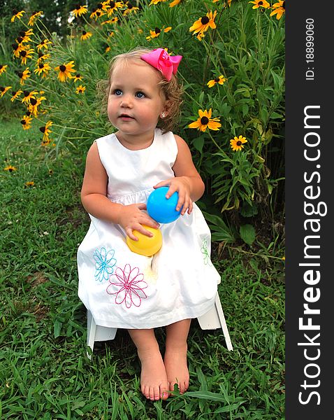 Little girl sitting on a stool outside on a beautiful sunny day holding a blue and yellow ball