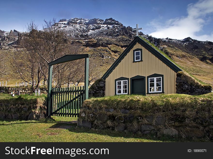 Icelandic wooden church with grass on roof in front of mountain backdrop