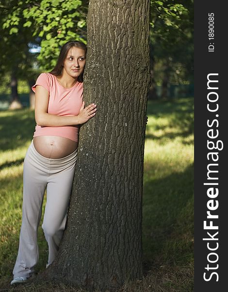 Young pregnant woman is standing in the park near the tree