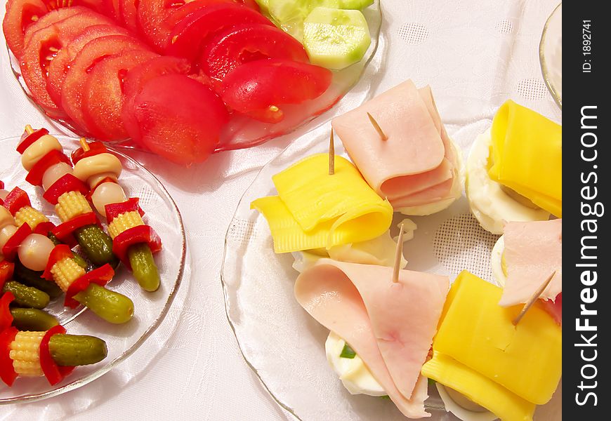 Piece of holiday supper table: tomato,cucumber,pickled cucumbers,cork,red paprika,onion,fungus,egg,cheese,ham on the plates,tablecloth