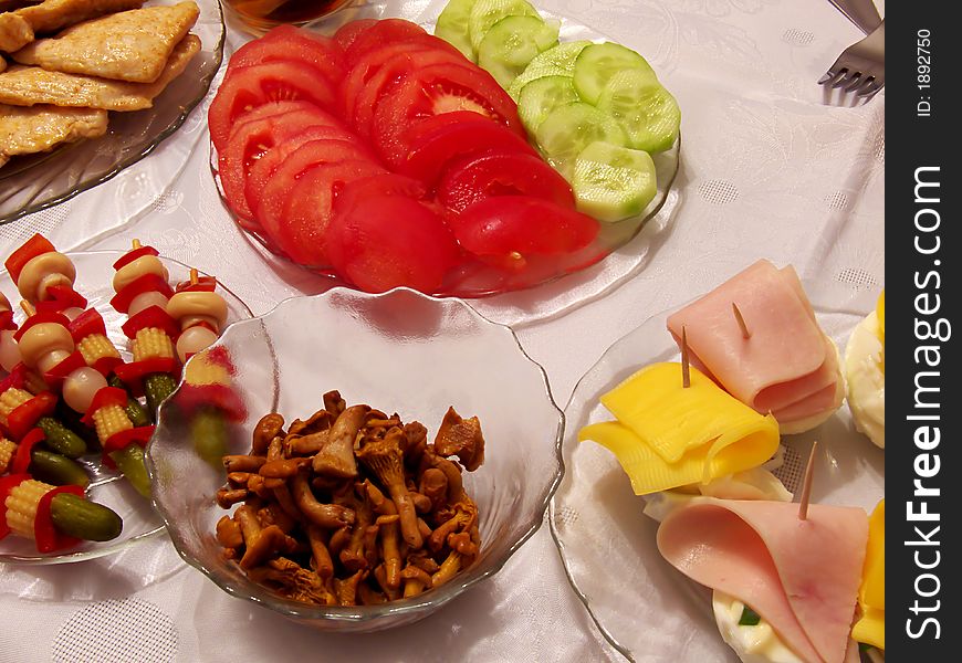 Piece of holiday supper table: tomato, cucumber, pickled cucumbers, cork, paprika, onion, fungus, egg, cheese, ham, poultry chop on the plates, all and fork on the tablecloth