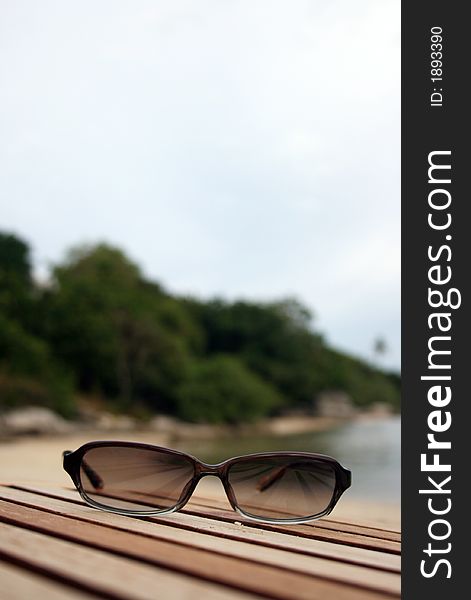 A pair of sunglasses on a wooden deck at the beach.