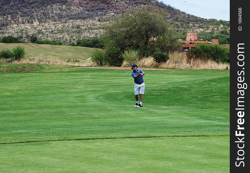 Golfer on the South African golf course pitching the ball onto the green. Golf club is in motion and the ball is in the air. Golfer on the South African golf course pitching the ball onto the green. Golf club is in motion and the ball is in the air.