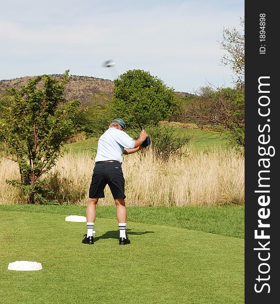 Golfer on the tee box. Golf club is in motion.