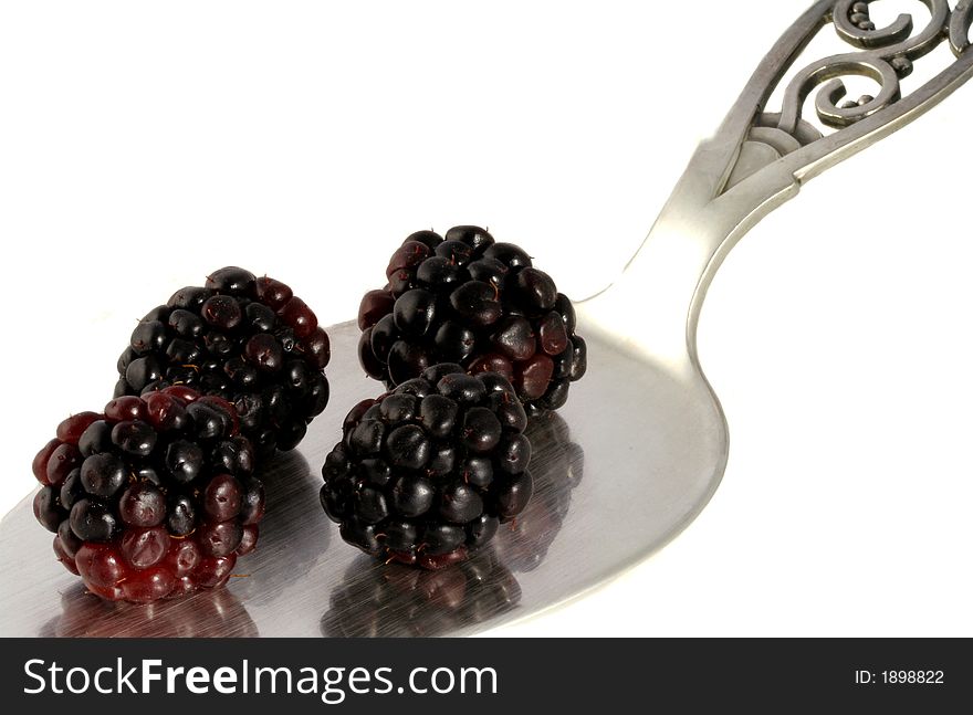 A silver pie server holds four juicy blackberries