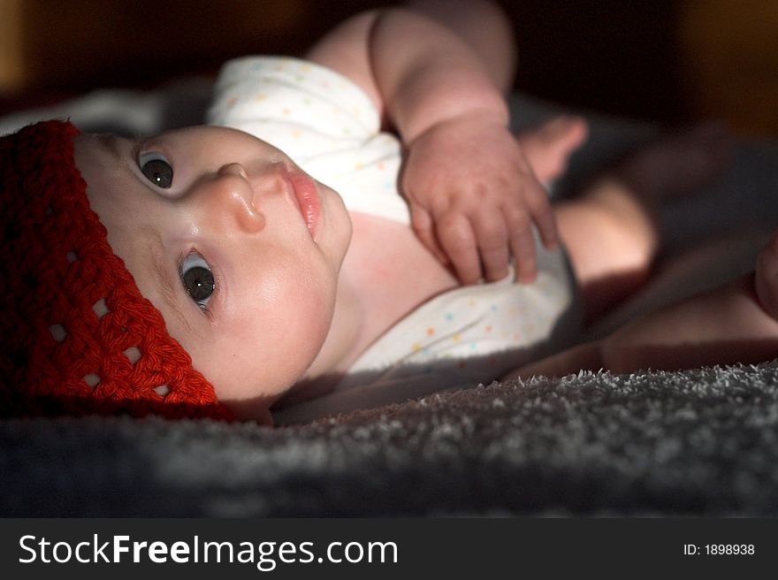 Image of baby wearing a red crochet cap, lying on a bed, lit by the setting sun. Image of baby wearing a red crochet cap, lying on a bed, lit by the setting sun