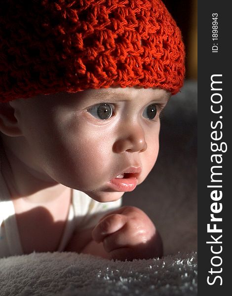 Image of baby wearing a red crochet cap, lying on a bed, lit by the setting sun. Image of baby wearing a red crochet cap, lying on a bed, lit by the setting sun