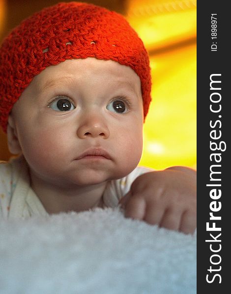 Image of baby wearing a red crochet cap, lying on a bed, lit by the setting sun. Image of baby wearing a red crochet cap, lying on a bed, lit by the setting sun