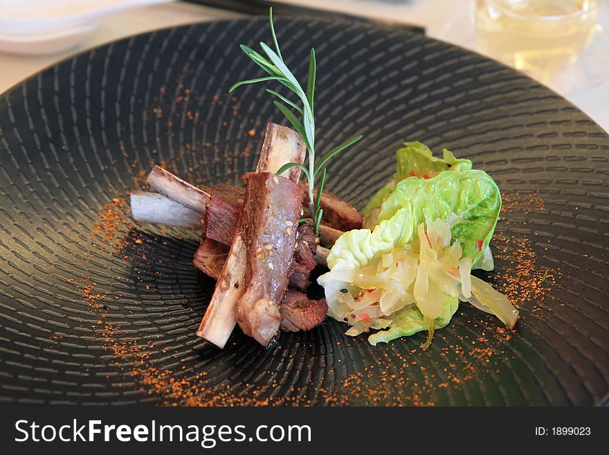 Roasted cuisine lamb ribs with lettuce leaves on a unique stone-black spiral plate