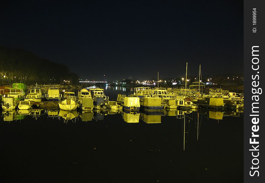 Boats on Belgrade river Sava, near lake, during the night. In background, you can see the lights of the city. Image is taken during very warm winter. Boats on Belgrade river Sava, near lake, during the night. In background, you can see the lights of the city. Image is taken during very warm winter.