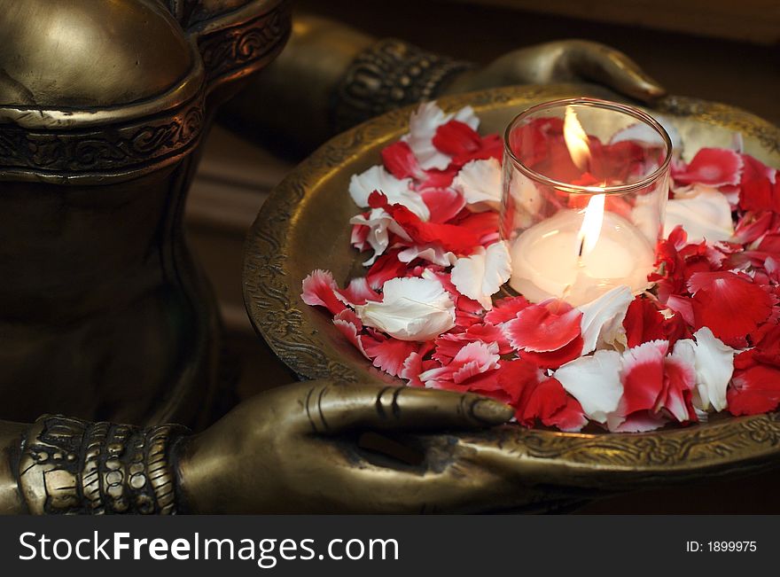 Detail of a deity sculpture with a candle adorned by red and white flower petals. Detail of a deity sculpture with a candle adorned by red and white flower petals.